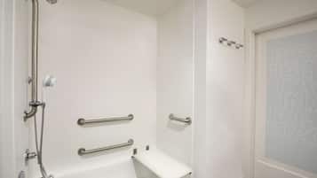 A bathroom with a white bathtub, grab bars, and a showerhead.