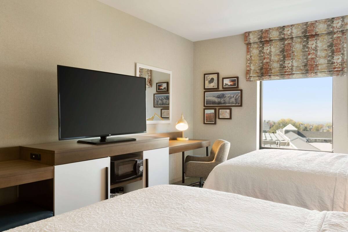 Habitación de hotel con dos camas, un televisor, un escritorio con lámpara y cuadros en la pared.