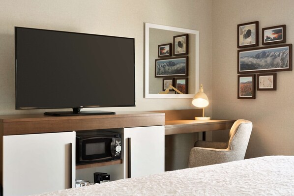 Habitación de hotel con cama, televisión, escritorio con lámpara, silla, microondas y cuadros en la pared.