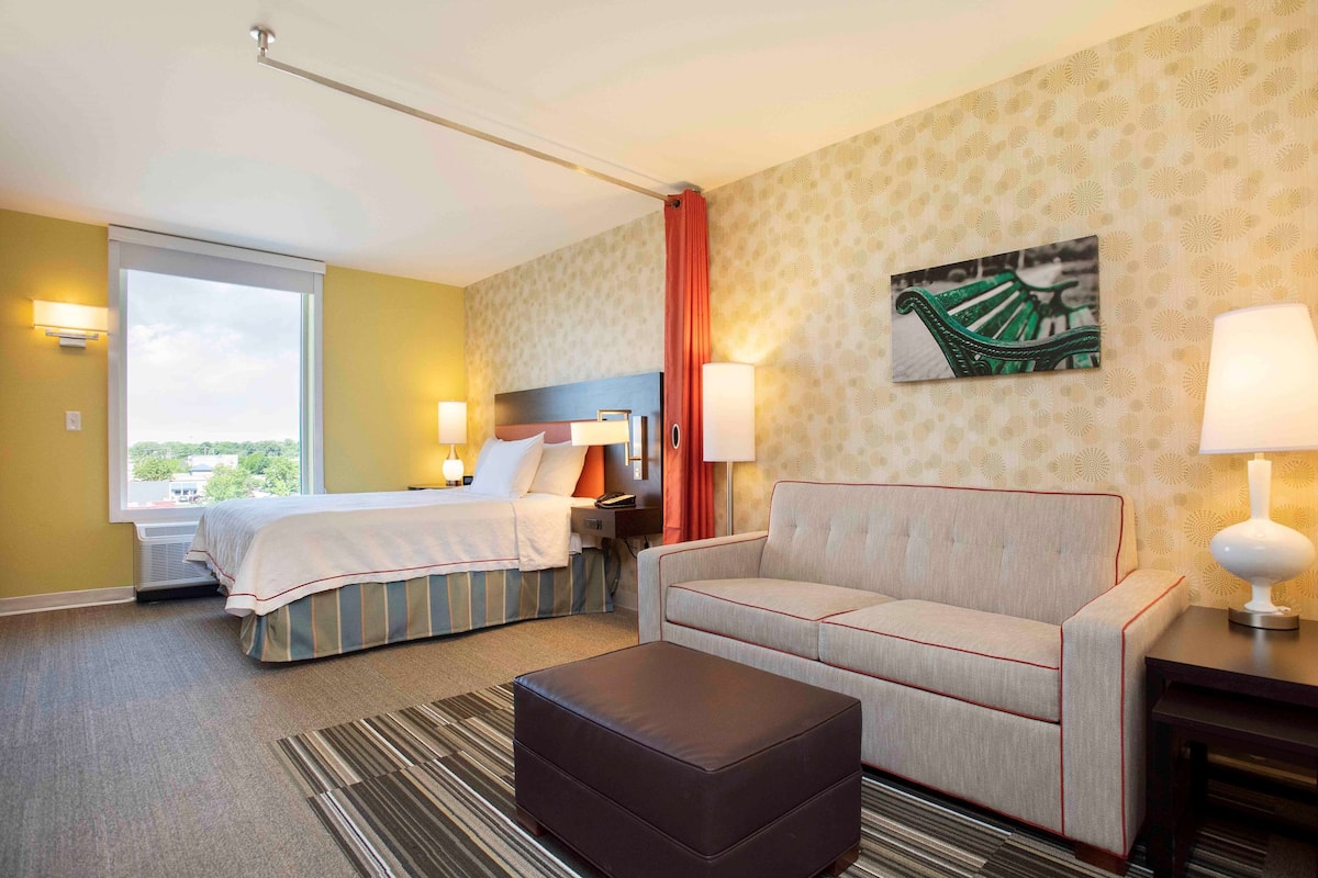 Una habitación de hotel con cama, sofá, una mesita y ventana con vistas.