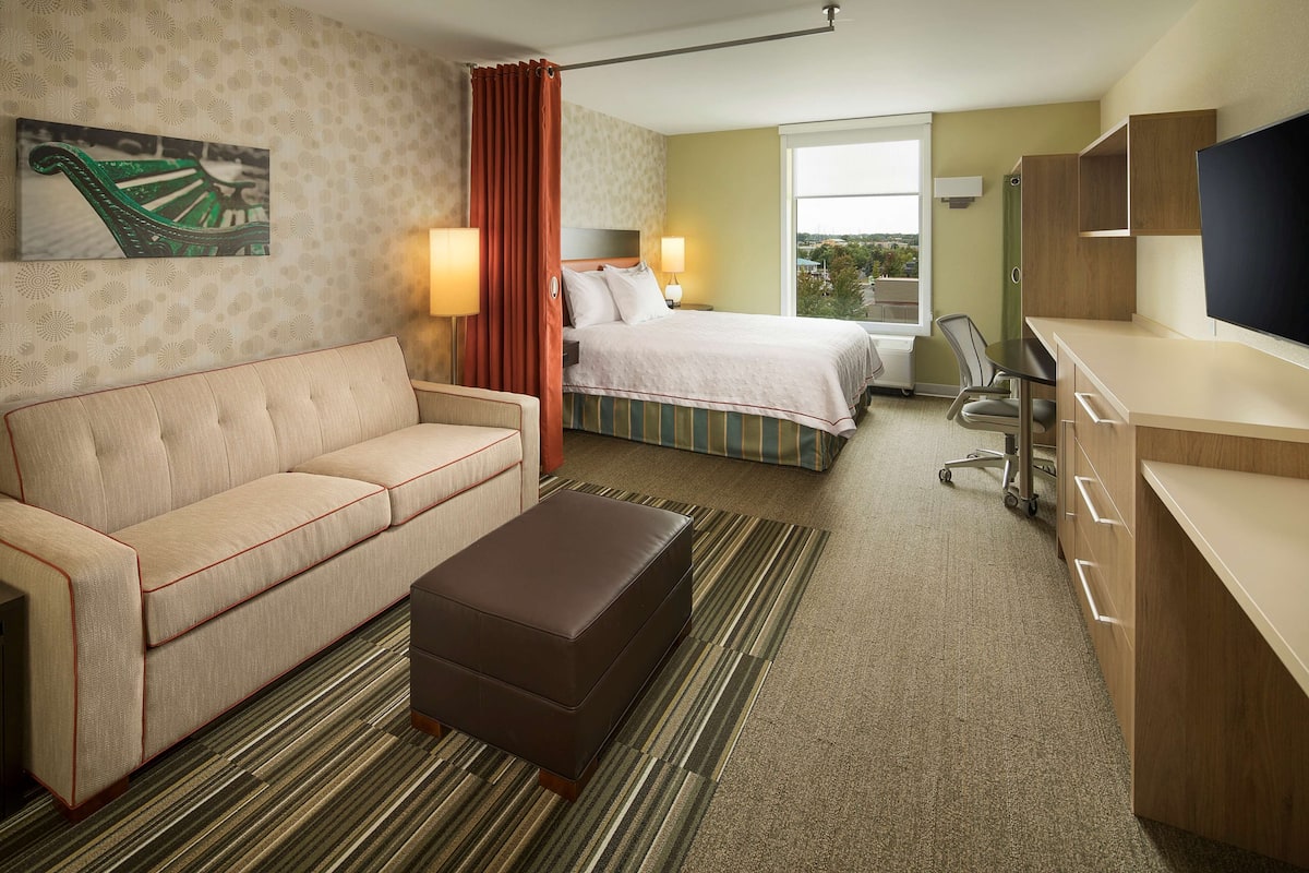 Habitación de hotel con cama, sofá, escritorio, televisor y ventana con vistas.
