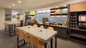 A modern breakfast area with a long counter, multiple chairs, and a coffee station. - Home2 Suites by Hilton Mishawaka South Bend, IN (Mishawaka)