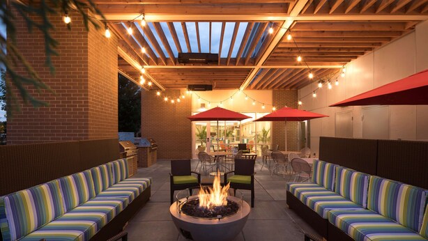 An outdoor patio with a fire pit, seating areas, and string lights. - Home2 Suites by Hilton Mishawaka South Bend, IN (Mishawaka)