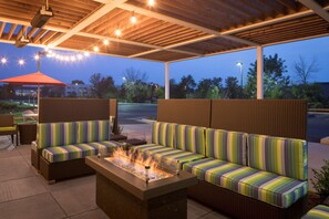 An outdoor seating area with a fire feature, wicker furniture, and string lights. - Home2 Suites by Hilton Mishawaka South Bend, IN (Mishawaka)