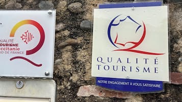 Dos señales colocadas en una pared de piedra, una con un logotipo y texto en francés, y la otra con un logotipo y texto en inglés, ambas relacionadas con la calidad turística.