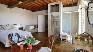 A bedroom with a wooden ceiling, a bed, a bedside table with a lamp, a potted plant, and a chair.