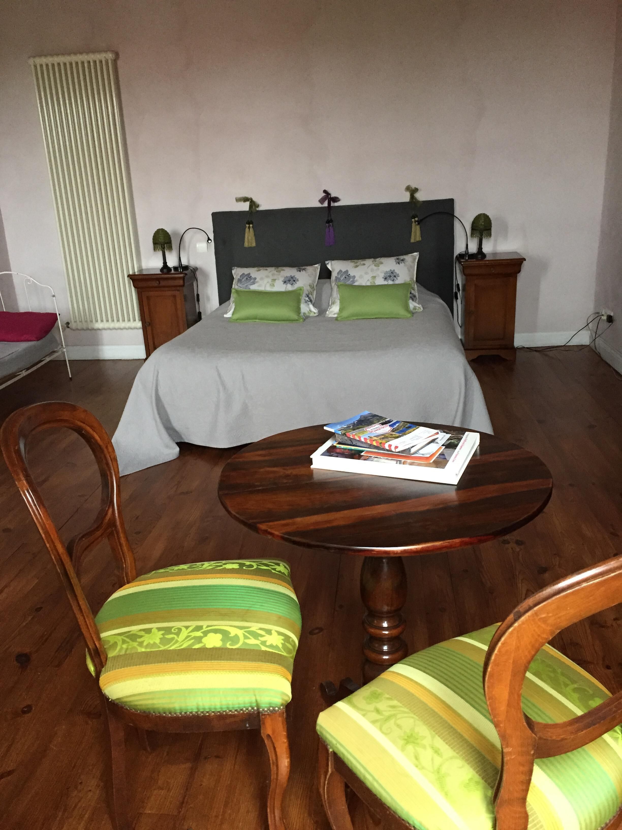 A bedroom with a bed, two bedside tables, a nightstand, a round wooden table, two chairs, and a radiator.