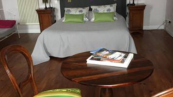A bedroom with a bed, two bedside tables, a nightstand, a round wooden table, two chairs, and a radiator.