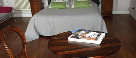 Un dormitorio con una cama, dos mesitas de noche, una mesita auxiliar, una mesa redonda de madera, dos sillas y un radiador.