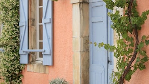 A building with a pink facade, blue shutters, and a garden with red flowers.