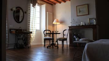 Una habitación con suelo de madera, una mesa con sillas, una cama, un espejo, una lámpara y una chimenea.