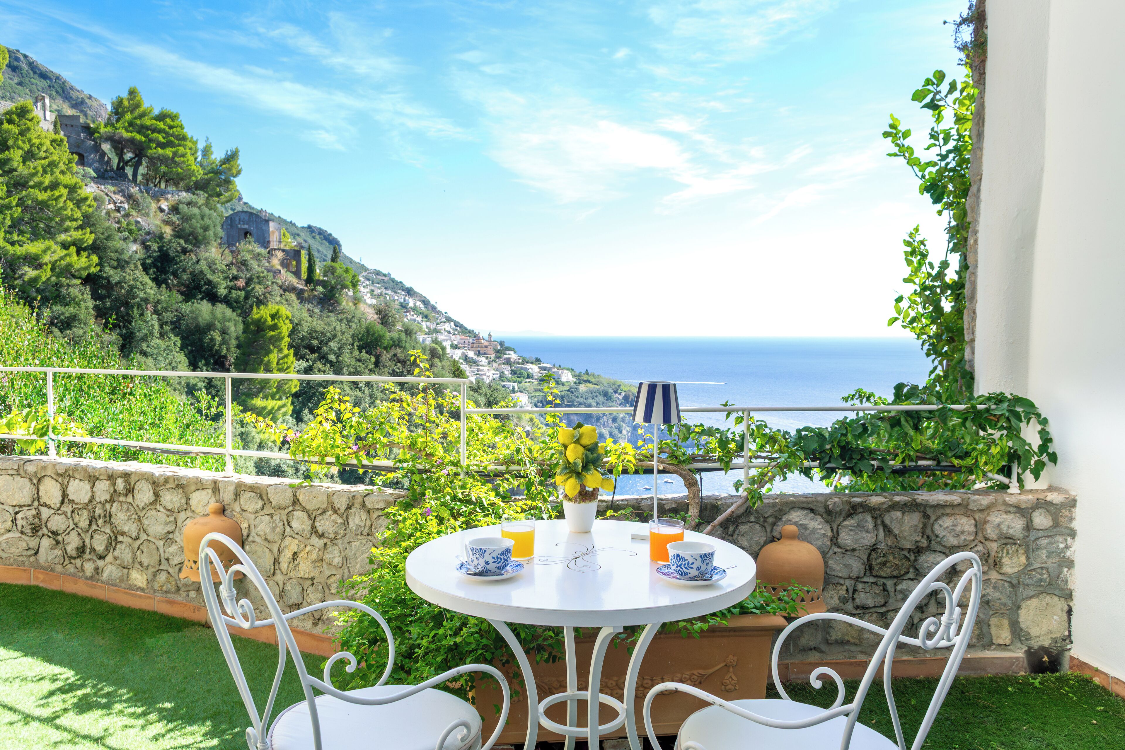 Una terraza con una mesa y sillas blancas, una planta en maceta y vista al mar.