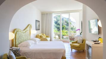 Habitación de hotel con una cama grande, un sofá, una silla, un escritorio y un balcón con vistas a zonas verdes.