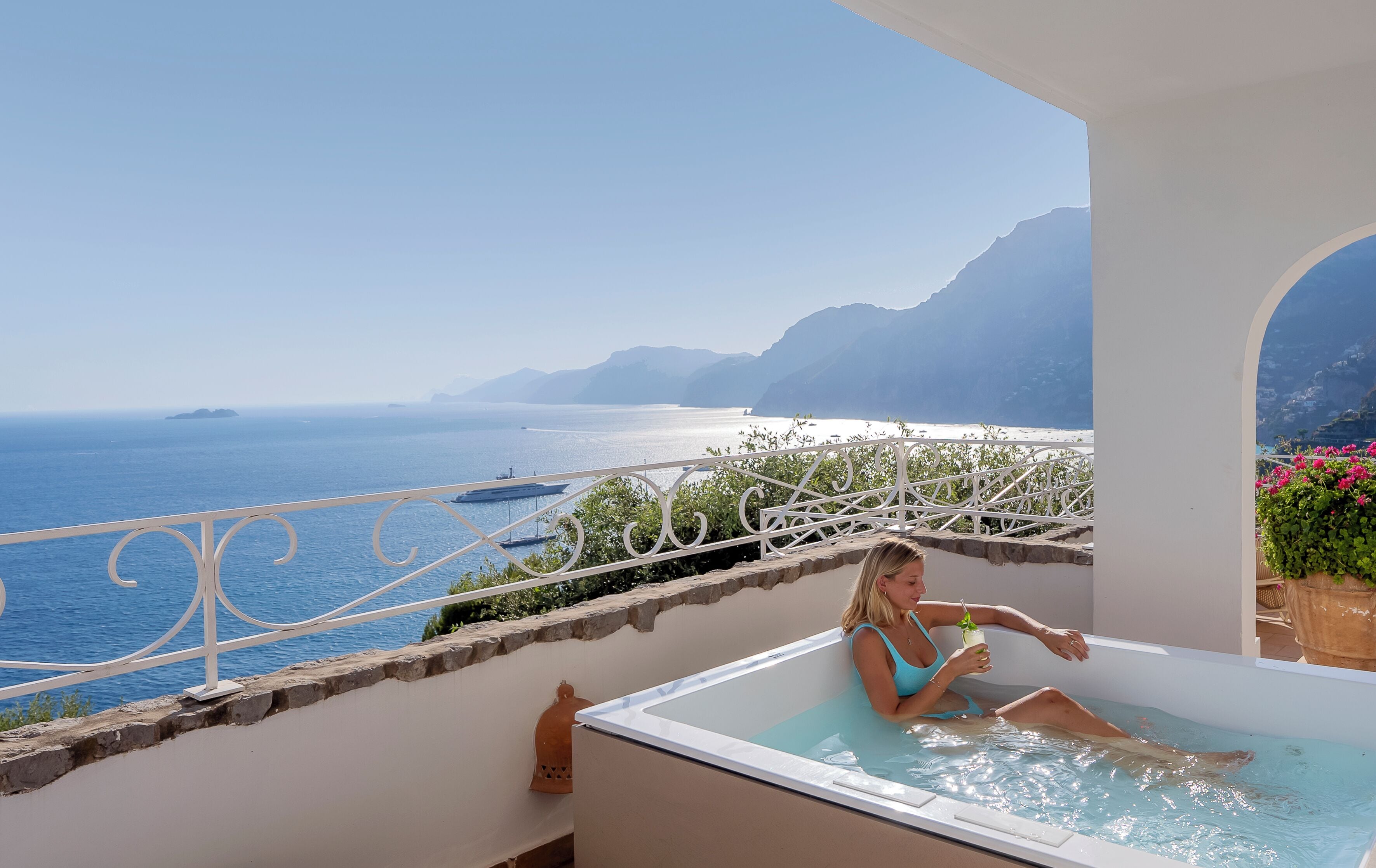 Una mujer descansando en un jacuzzi con vistas al océano y montañas.