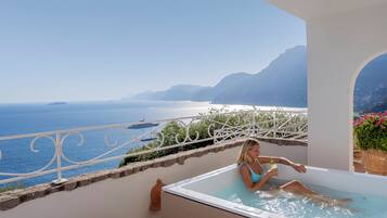 Una mujer descansando en un jacuzzi con vistas al océano y montañas.