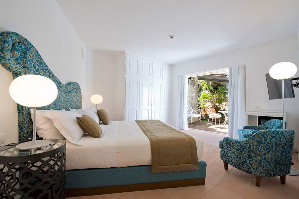 A bedroom with a bed, bedside table, chair, and a view of an outdoor area.