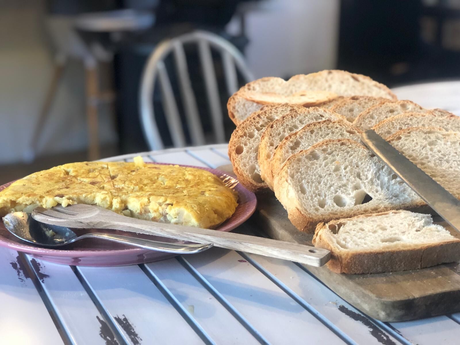 A table with a plate of sliced bread and a piece of quiche.