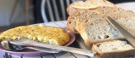 A table with a plate of sliced bread and a piece of quiche.
