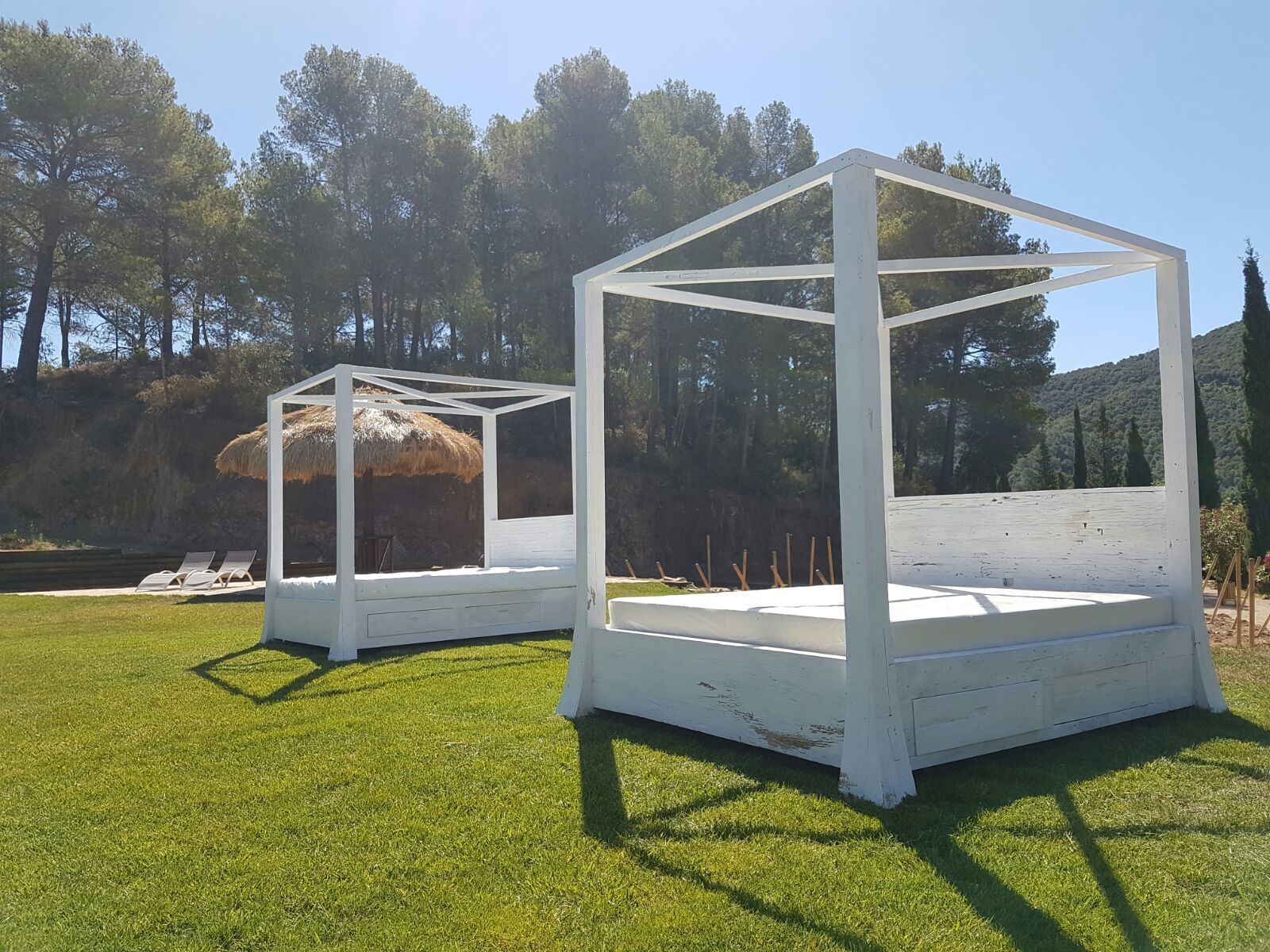 Two white, open-air structures with a simple, geometric design, set on a grassy area with trees in the background.