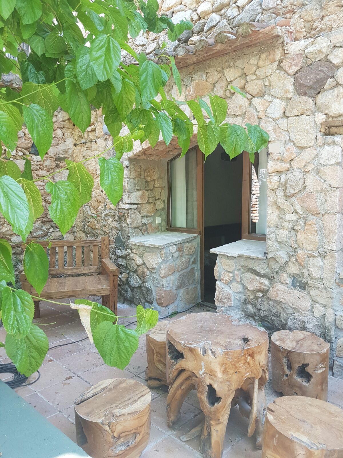 Edifici de pedra amb una banca de fusta i una taula amb tamborets.