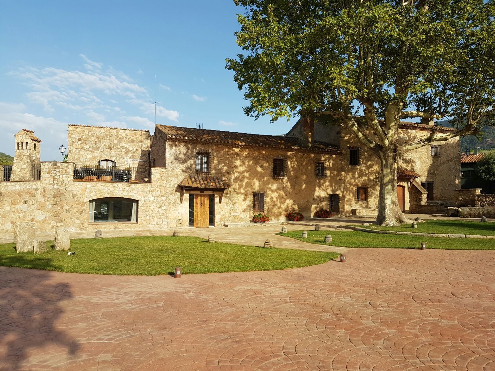 A stone building with a courtyard, a large tree, and a clear sky.