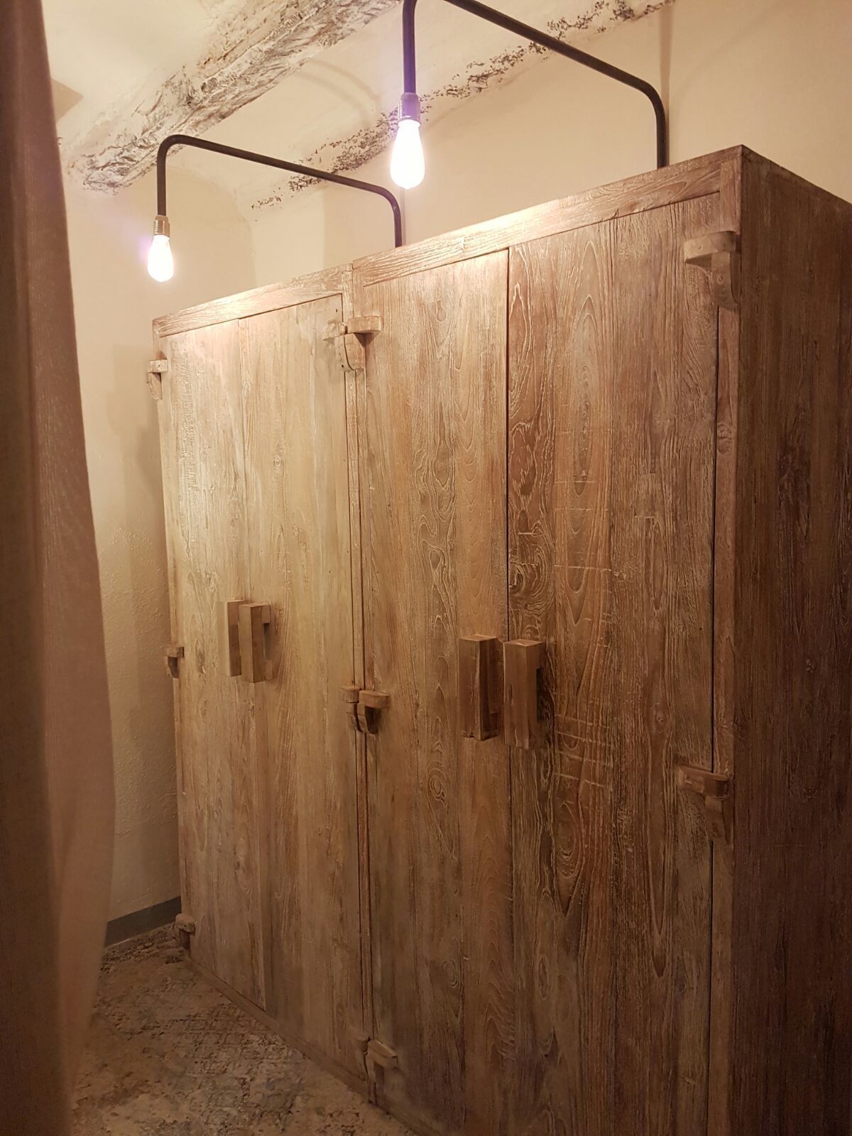 A wooden wardrobe with two doors and a hanging rod, illuminated by three light bulbs.