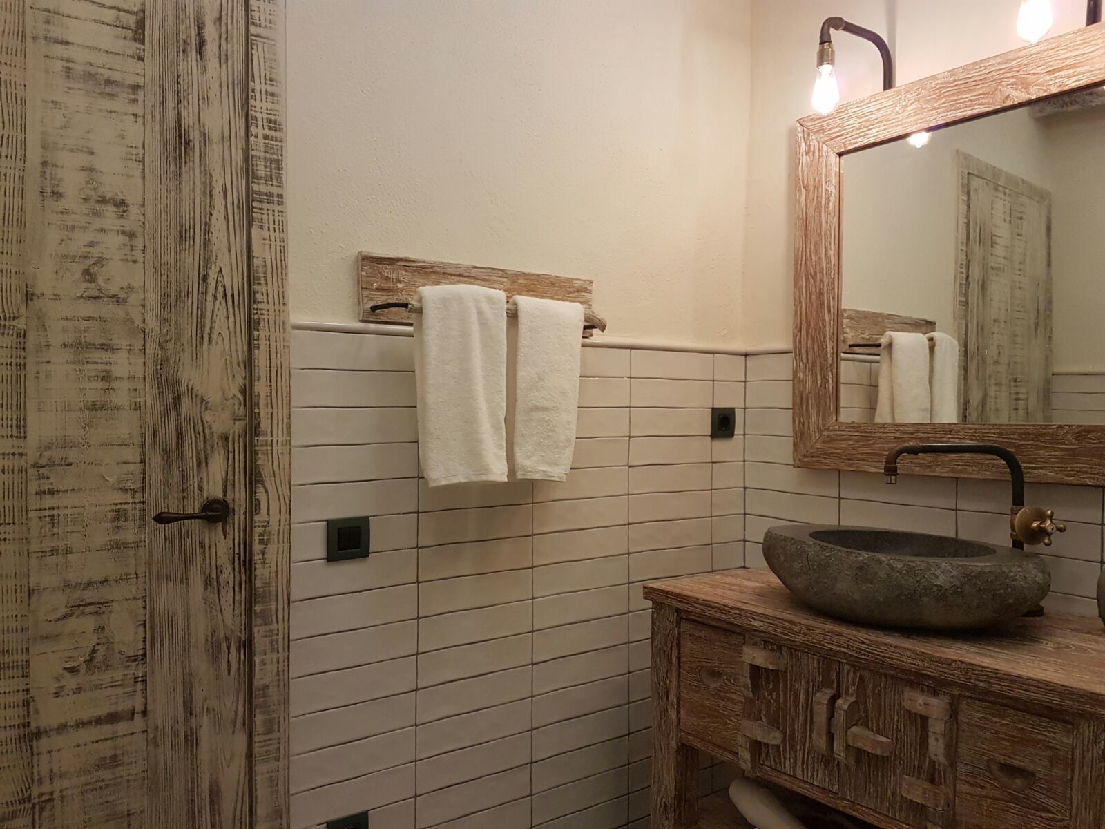 A bathroom with a rustic wooden door, a stone sink, and a mirror with a wooden frame.