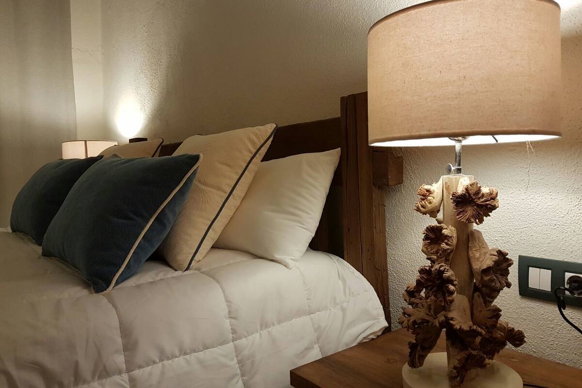 A bed with a white and blue pillow arrangement, a wooden headboard, and a lamp with a textured base.