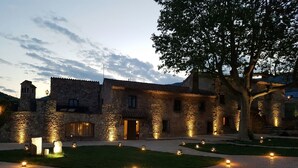 A stone building with multiple doors and windows, surrounded by a paved courtyard with evenly spaced lights. - Mas del Sord 1335 (L'Albiol)