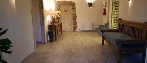 Un pasillo con un arco de piedra, un banco de madera, una mesa con lámpara y una mesa de vidrio con plantas verdes.