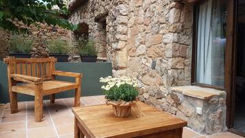 A wooden bench and table set on a tiled patio with a stone wall and potted plants.