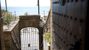 A view through a gate with a metal fence, a stone wall, and a street leading to the sea. - Sundial House Beachfront Arts & Crafts Period House (Lyme Regis)