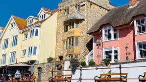 A row of colorful buildings with stone facades and thatched roofs, featuring outdoor seating areas. - Sundial House Beachfront Arts & Crafts Period House (Lyme Regis)