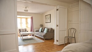 A living room with a wooden floor, a sofa, a chair, a coffee table, and a lamp. - Sundial House Beachfront Arts & Crafts Period House (Lyme Regis)