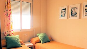 A room with two single beds, a small table, a window with blinds, and three framed pictures on the wall. - Cute and quiet, in the city center, paid parking (Sevilla)