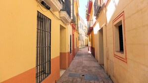 A narrow alleyway with yellow and orange buildings, barred windows, and a tiled floor. - Cute and quiet, in the city center, paid parking (Sevilla)