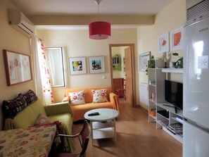 Un salon avec un canapé, une petite table, un téléviseur et un réfrigérateur.