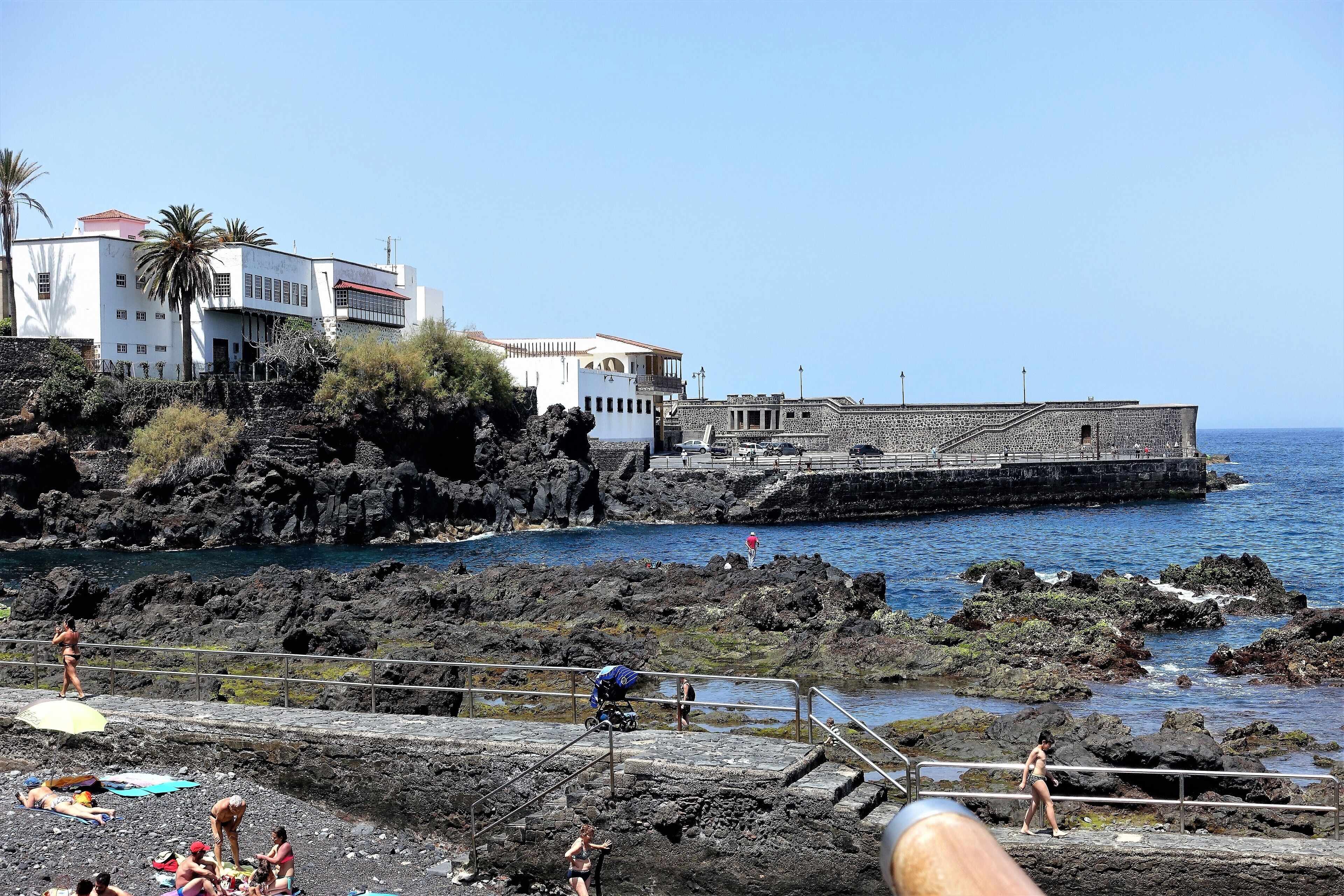 Zona costera con terreno rocoso, un muelle y edificios.