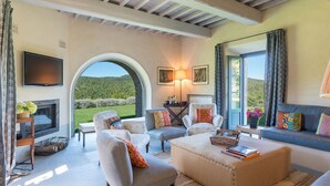 A spacious living room with a fireplace, comfortable seating, and a large window offering a view of the outdoors. - Muffato 6, Emma Villas (Sarteano)