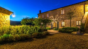 A stone building with a gravel courtyard, a wooden gate, and a pathway leading to the entrance. - Muffato 6, Emma Villas (Sarteano)
