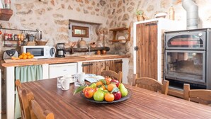 Una cocina rústica con pared de piedra, armarios de madera, horno empotrado y una mesa de comedor con fruta.