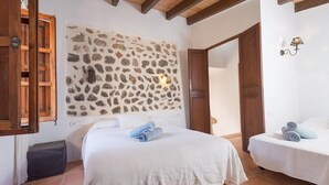 Un dormitorio con dos camas, una pared de piedra, vigas de madera y suelo de baldosas.
