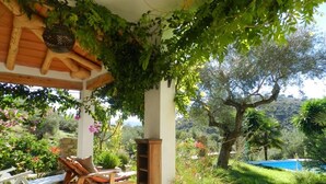 Un espacio de estar al aire libre con techo, mobiliario de madera, una pérgola cubierta de plantas trepadoras y vistas a una piscina y follaje.