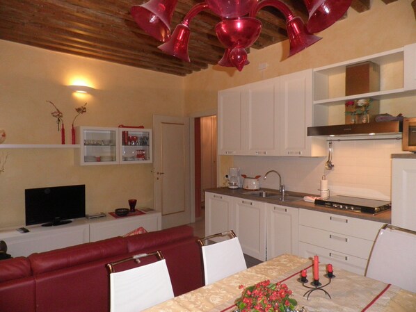 A compact living space with a red sofa, a dining table with candles, a kitchen area, and a television in the corner. - Near Ponte di Rialto, fish and fruit market, all kinds of shops (Venezia)