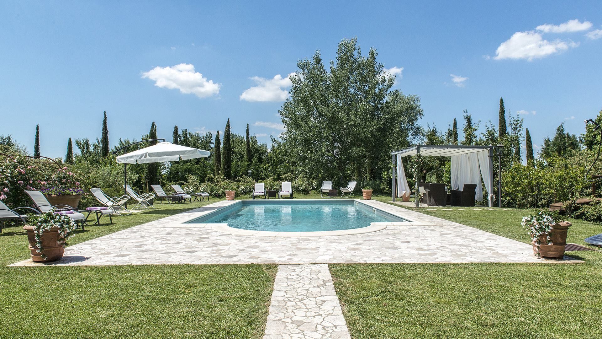 Une piscine avec des chaises longues et une pergola, le tout aménagé dans un jardin paysager.