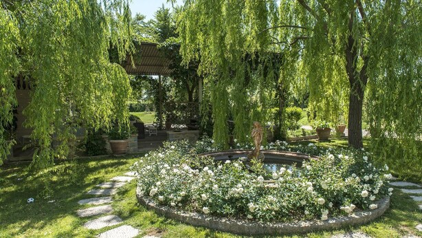 Un jardín con un parterre circular, una estatua y una pérgola.