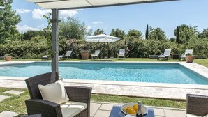 Una piscina con sillas de descanso y una mesa con una botella y vasos.