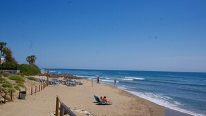 Een strand met ligbedden, parasols, een houten hek en de oceaan.