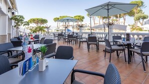 Een terras met tafels en stoelen, parasols en potplanten.