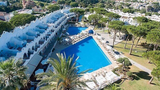 Een resort met een groot zwembad, een overdekt terras met zitplaatsen en uitzicht op zee.